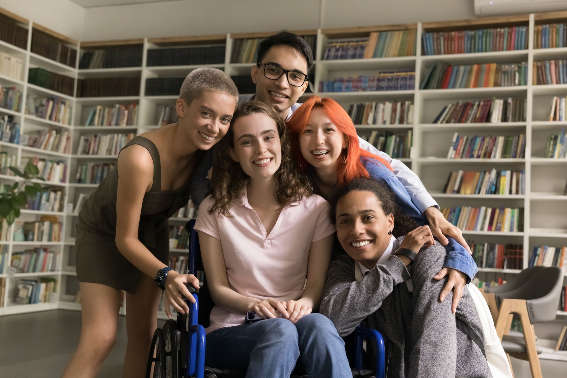 Portrait of diverse schoolmates hugging posing for camera in library
